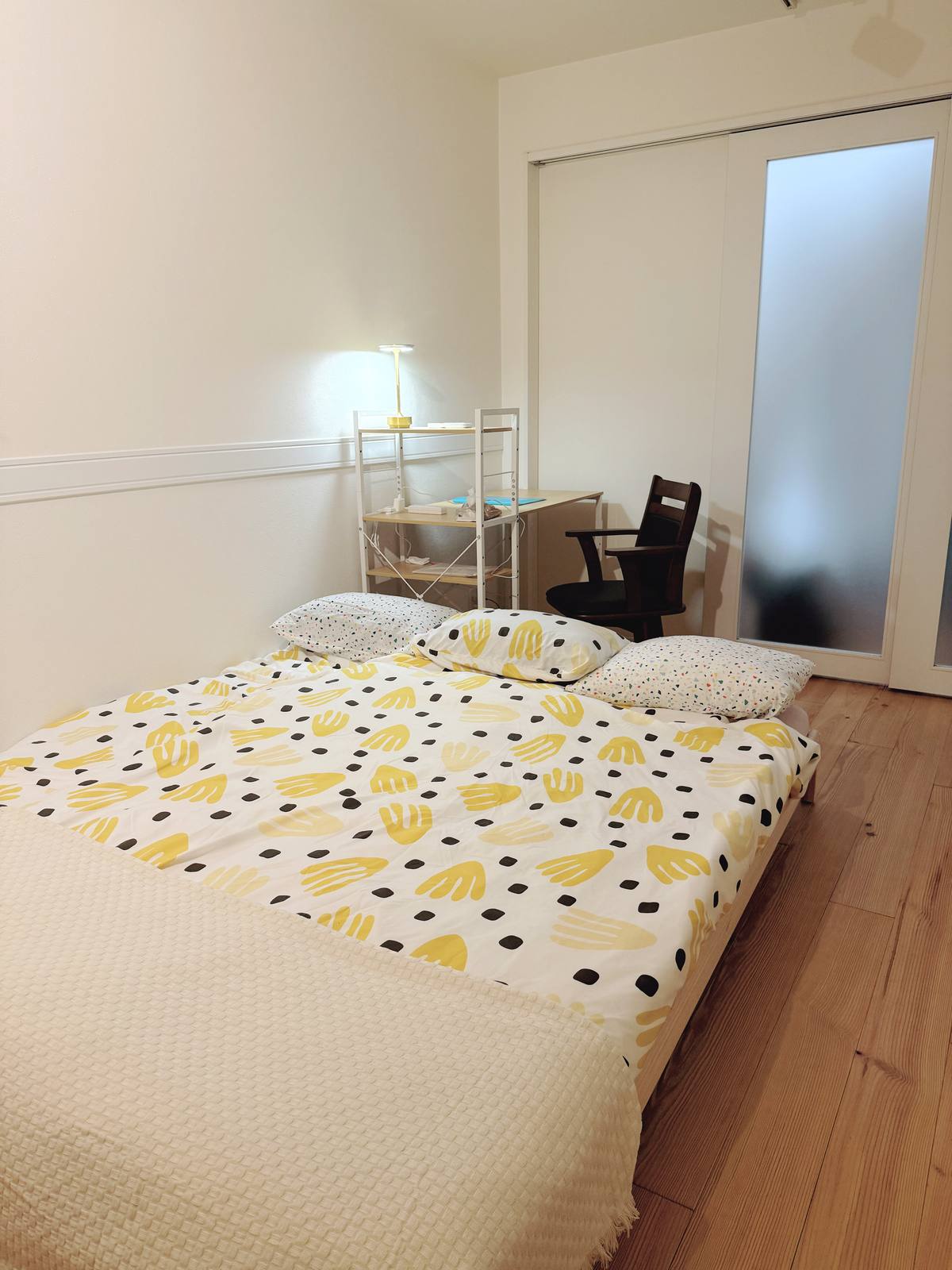 A calm bedroom with yellow-patterned bedding and warm wood floors.