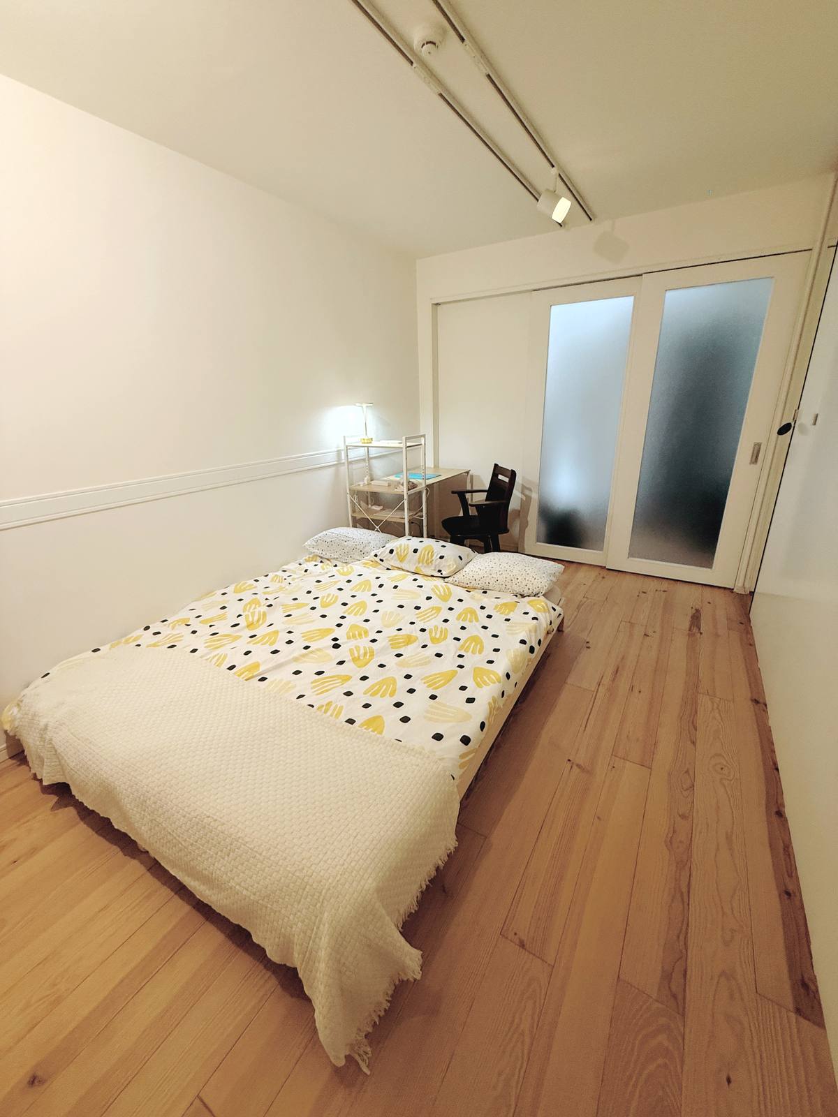 A calm bedroom with yellow-patterned bedding, a desk and warm wood floors.